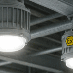 Luminárias à prova de explosão instaladas no teto metálico de uma estrutura industrial, com luz branca intensa em ambiente interno.