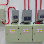 Sistema de detecção de fumaça com painéis e controladores instalados em parede, incluindo três módulos cinza, conduítes vermelhos e caixas de controle elétrico, utilizado em ambientes industriais para monitoramento de incêndios.