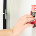 Manutenção preventiva em sistema de alarme de incêndio, com técnico acionando manualmente um acionador de emergência para teste e verificação do funcionamento do equipamento.